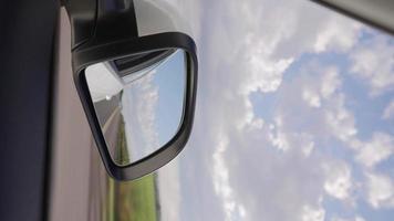 video vertical, vista de espejo lateral de un camión que acelera por la carretera en un hermoso día nublado. ir a todas partes concepto de viaje en vehículo.