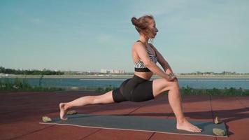 joven atlética haciendo yoga en el fondo de un lago. hermosa chica está haciendo ejercicio al aire libre. ejercicios de estiramiento y flexibilidad video