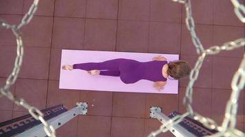 Young athletic woman in a sports purple tracksuit does exercise for stretching. Fitness outdoors. Slow motion. Top view through a basketball hoop video