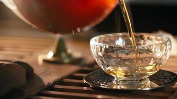 Herbal Chinese Tea Poured into Beautiful Transparent Glass against background of the smoke coming from scented sticks, backlit by warm light. Tea ceremony. Oriental cup close up. Unrecognizable person video