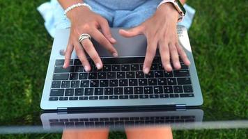 top naar beneden visie van een vrouw typen Aan een laptop toetsenbord terwijl zittend buiten Aan de gras video