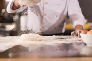 chef sprinkling flour over fresh pizza dough photo