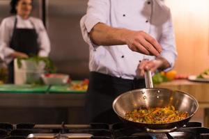 chef putting spices on vegetables in wok photo