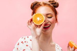 Young energetic red-haired girl in white T-shirt holding tasty oranges on pink background photo