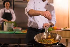 chef putting spices on vegetables in wok photo