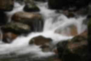 vista borrosa de la cascada en el arroyo con rocas en el bosque foto