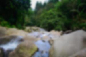 vista borrosa de la cascada en el arroyo con rocas en el bosque foto