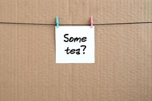 Some tea Note is written on a white sticker that hangs with a clothespin on a rope on a background of brown cardboard photo