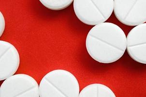 A few white tablets lie on a bright red background surface. Background image on medical and pharmaceutical topics photo