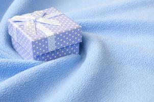 A small gift box in blue with a small bow lies on a blanket of soft and furry light blue fleece fabric with a lot of relief folds. Packing for a gift to your lovely girlfriend photo