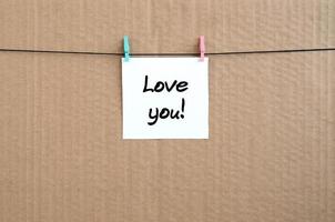 Love you Note is written on a white sticker that hangs with a clothespin on a rope on a background of brown cardboard photo