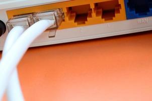 los enchufes del cable de Internet están conectados al enrutador de Internet, que se encuentra sobre un fondo naranja brillante. elementos necesarios para la conexión a internet foto