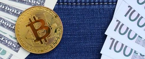 Golden Bitcoin, dollar and euro bills lies on a blue jeans fabric. New virtual money. New crypto currency in the form of the coins photo