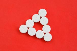 Several white tablets lie on a bright red background in the form of an even triangle. Background image on medicine and pharmaceutical topics photo