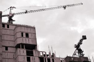 Working tall cranes inside place for with tall buildings under construction against a clear blue sky. Crane and building working progress. Retro tone photo