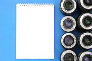 Several photographic lenses and white notebook lie on a bright blue background. Space for text photo