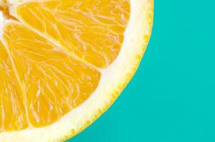 Top view of a one orange fruit slice on bright background in turquoise green color. A saturated citrus texture image photo