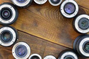 Several photographic lenses lie on a brown wooden background. Space for text photo