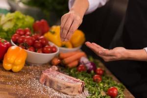 chef poniendo sal en una jugosa rebanada de bistec crudo foto