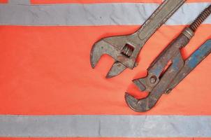 Adjustable and pipe wrenches against the background of an orange signal worker shirt photo