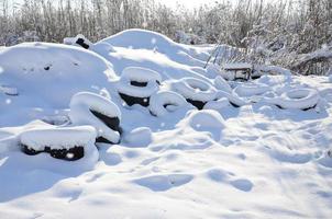 Used and discarded car tires lie on the side of the road, covered with a thick layer of snow photo