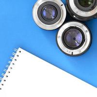 Several photographic lenses and white notebook lie on a bright blue background. Space for text photo