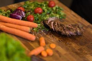 Juicy slices of grilled steak on wooden board photo