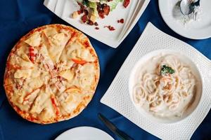 pizza hawaiana, ensalada césar y espaguetis de marisco endecha plana. mesa de vista superior de comida italiana. foto