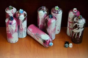 Still life with a large number of used colorful spray cans of aerosol paint lying on the treated wooden surface in the artist's graffiti workshop. Dirty and stained cans for spray art photo