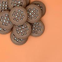 Detailed picture of dark brown round sandwich cookies with coconut filling on an orange surface. Background image of a close-up of several treats for tea photo