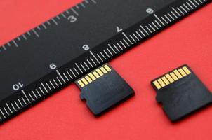 Two small micro SD memory cards lie on a red background next to a black ruler. A small and compact data and information store photo