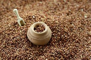 Background image of a large pile of buckwheat, in the middle of which lies a small jug and a wooden spatula for cereals photo