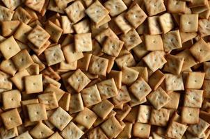 A lot of small cookies are square shaped. A pattern of a yellow salt cracker. Background image with salted pastry photo