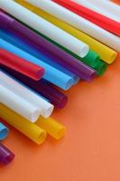 Many colorful straws for drinks lies on a bright orange background surface photo