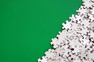 A pile of uncombed elements of a white jigsaw puzzle lies on the background of a green surface. Texture photo with copy space for text