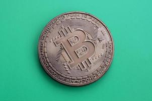 Chocolate product in the form of physical bitcoin lies on a green plastic background. Model of the crypto currency in the edible form photo