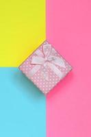 Small pink gift box lie on texture background of fashion pastel blue, yellow and pink colors paper in minimal concept photo