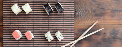 Sushi rolls and wooden chopsticks lie on a bamboo straw serwing mat. Traditional Asian food. Top view photo