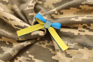 TERNOPIL, UKRAINE - SEPTEMBER 2, 2022 Ribbon with Ukrainian Coat of Arms and national flag colors on army camouflage uniform photo