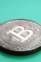 Chocolate product in the form of physical bitcoin lies on a green plastic background. Model of the crypto currency in the edible form photo