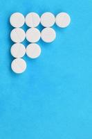 Several white tablets lie on a bright blue background in the form of a triangular arrow. Background image on medicine and pharmaceutical topics photo