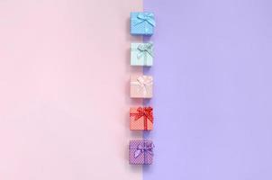 Small gift boxes of different colors with ribbons lies on a violet and pink color background photo