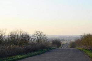 Dawn in the village. Asphalt road, leaving far into the distance among the fields photo
