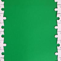 Fragment of a folded white jigsaw puzzle on the background of a green plastic surface. Texture photo with copy space for text