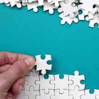 The hand folds a white jigsaw puzzle and a pile of uncombed puzzle pieces lies against the background of the blue surface. Texture photo with space for text