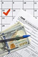 1040 Individual Income Tax Return blank with dollar bills, calculator and pen on calendar page with marked 15th April photo