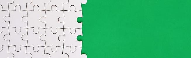 Fragment of a folded white jigsaw puzzle on the background of a green plastic surface. Texture photo with copy space for text