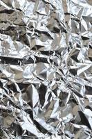 Thin wrinkled sheet of crushed tin aluminum silver foil background with shiny crumpled surface for texture photo