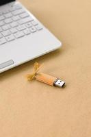 Orange usb flash memory card with a bow lies on a blanket of soft and furry light orange fleece fabric beside to a white laptop. Classic female gift design for a memory card photo