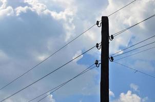 Old wooden electric pole for transmission of wired electricity on a background of a cloudy blue sky. Obsolete method of supplying electricity for later use photo